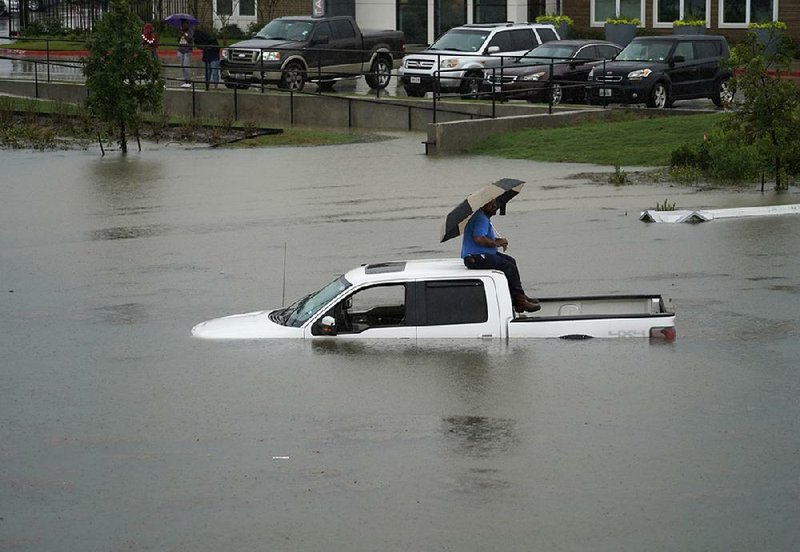 A man sits atop a truck Thursday on a flooded road in Houston. 