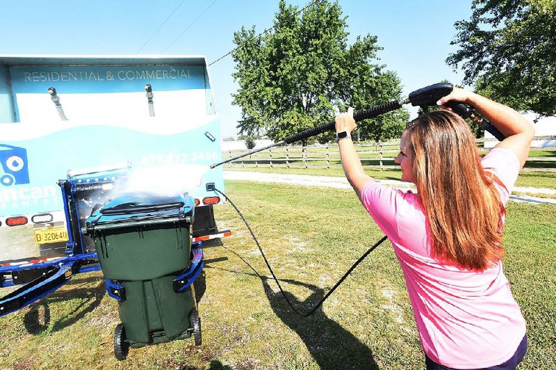 Heather Reynolds of Lowell power washes the outside of a trash can last week. Her business, Can Can Cleaning, has been up and running for about six months, washing residential trash bins and recycling containers. 