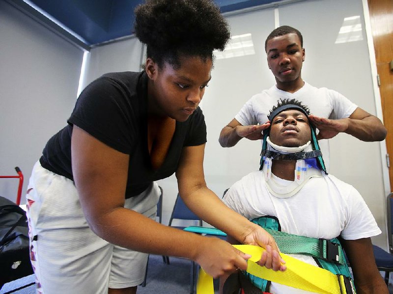 Students Naja Lowe (left) and Brelynn Bryant practice putting classmate James Allen in a Kendrick Extrication Device during the emergency medical services class Thursday at the Metropolitan Career-Technical Center in Little Rock. 