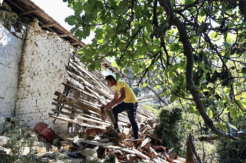 A man removes debris from a damaged house Sunday in Albania’s Zhurje village.
