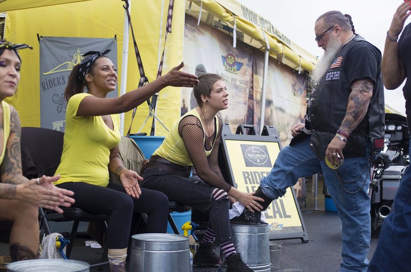 Nicki Jo (from left) of Mitchell, S.D., and Christina Martinez of Fort Lauderdale, Fla., call over customers Thursday for boot weather-sealing as Jade Boston of Greeneville, S.C., polishes the boots of J.J. Brock of Lonejack, Mo., during a Bikes, Blues &amp; BBQ Festival at Pig Trail Harley-Davidson in Rogers. Rally officials say Bikes, Blues &amp; BBQ is the world's largest charity motorcycle rally benefiting women, children and underserved members of the Northwest Arkansas. NWA Democrat-Gazette/CHARLIE KAIJO