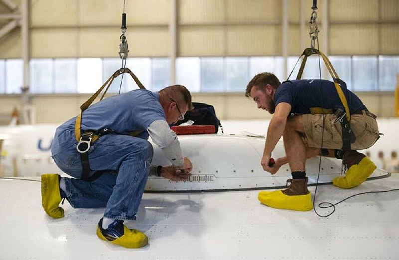 Bradley Gangstad (left), a mechanic at AAR Corp., and student Kieran Cummings work to attach a dome protecting radar equipment on top of a commercial airplane in Duluth, Minn. 