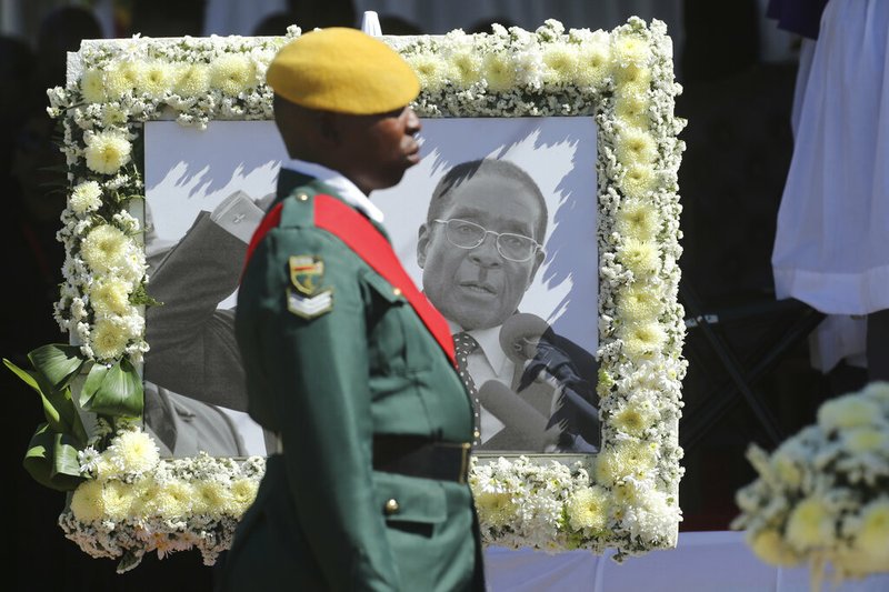 A soldier stands next to a portrait of former Zimbabwean President Robert Mugabe during mass at his rural home in Zvimba, about 100 kilometers north west of the capital Harare, Saturday. Sept, 28, 2019. According to a family spokesperson Mugabe is expected to be buried at the residence after weeks of drama mystery and contention over his burial place.