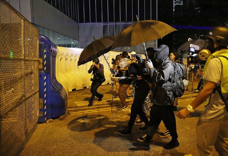 Protesters, some clad in black, outfitted in goggles and masks approach barricades Saturday outside government offices in Hong Kong. 