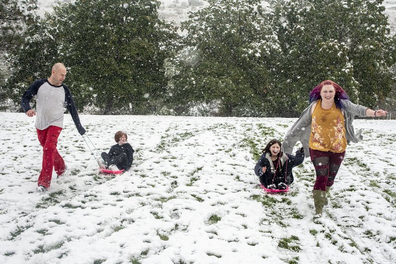 Tommy Little, from left, Cody Little, Kyndra Neal and Tanya Little use the snow accumulation to sled down a hill in Missoula, Mont., Sunday, Sept. 29, 2019. Montana Gov. Steve Bullock declared an emergency Sunday, allowing the state to mobilize resources to help affected areas. (Ben Allan Smith/The Missoulian via AP)
