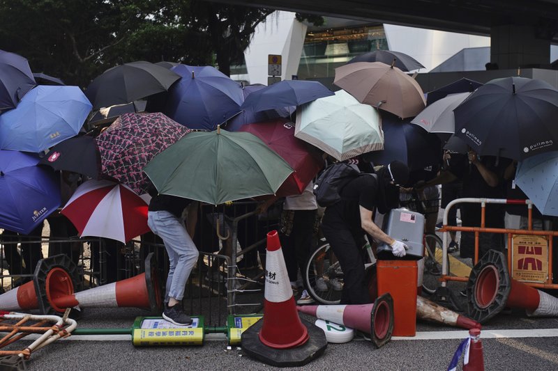 Protesters hide behind umbrellas as they form a barricade to block a road in Hong Kong on Friday, Oct. 4, 2019. Thousands of protesters in masks are streaming into Hong Kong streets after the territory's leader invoked rarely used emergency powers to ban masks at rallies. (AP Photo/Felipe Dana)

