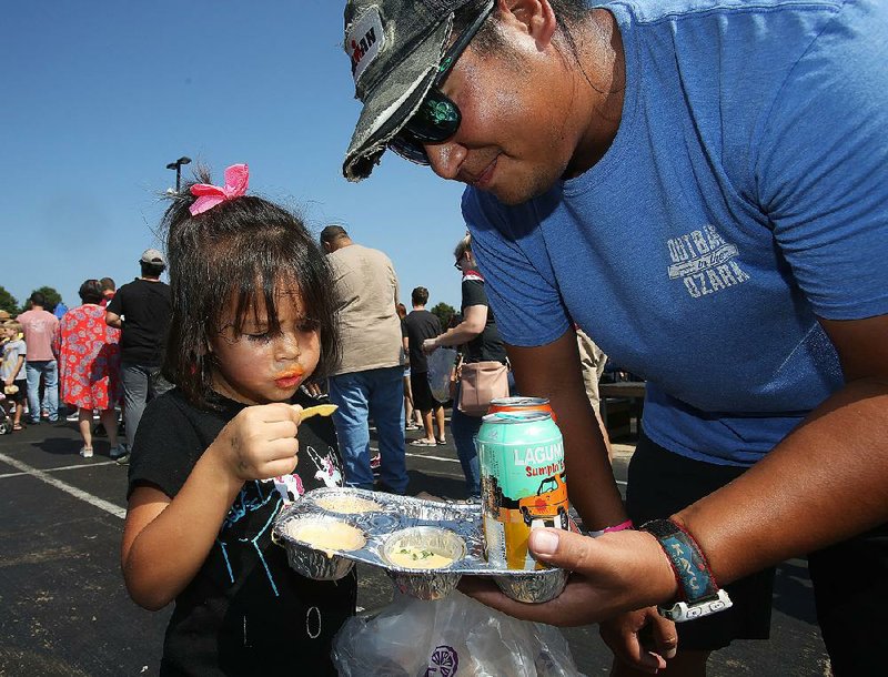 And Xaysuda, 4, of Maumelle munches on cheese dip while her father, Adam, holds the tray for her during the ninth annual World Championship Cheese Dip Championship on Saturday at the Clinton Presidential Center in Little Rock. For more photos are available at arkansasonline.com/106cheese/ 