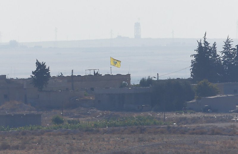 In this photo taken from the Turkish side of the border between Turkey and Syria, in Akcakale, Sanliurfa province, southeastern Turkey, a flag of Kurdish People's Protection Units, or YPG, flies on a building in the Syrian town of Tel Abyad, Tuesday, Oct. 8, 2019. Turkey's vice president says his country won't bow to threats in an apparent response to U.S. President Donald Trump's warning to Ankara about the scope of its planned military incursion into Syria aiming to create a zone that would allow Turkey to resettle Syrian refugees there. (AP Photo/Lefteris Pitarakis)