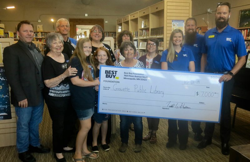 Westside Eagle Observer/SUSAN HOLLAND Gravette Mayor Kurt Maddox, Gravette Public Library manager Karen Benson, library staff members, and members of the Greater Gravette Chamber of Commerce gather Tuesday, Oct. 1, to accept a $7,000 grant check from the Best Buy Community Foundation. Pictured are Mayor Maddox (left, front), Mary Kay Kelley, library patrons Rebekah and Naomi Vanlandingham, Kathryn Johnson, Santana Mead, manager of the Rogers Best Buy store Barry Hastings, Chamber president Fred Overstreet (left, rear), Karen Benson, Cathy Crawford, Brittany Mangold and Erik Burkland.