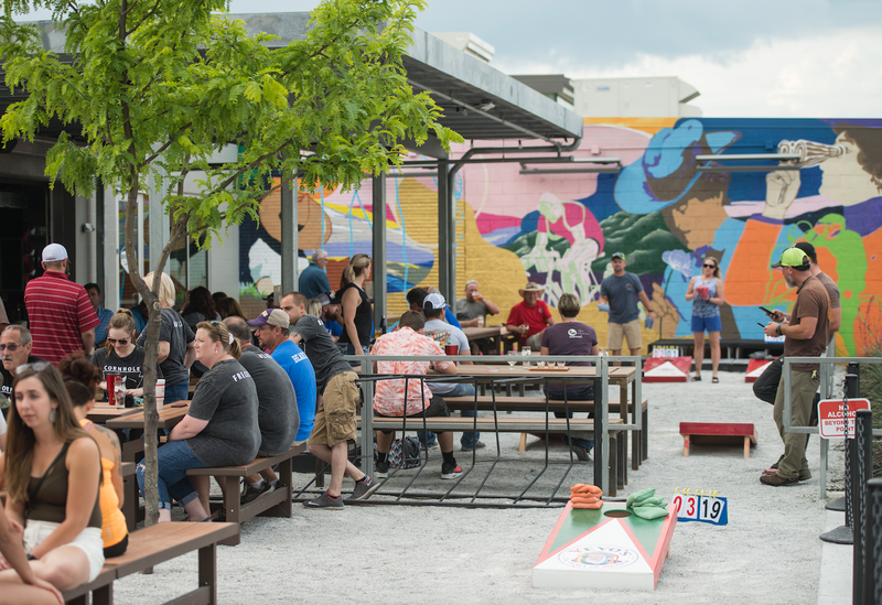 Guests play in the weekly cornhole tournament Tuesday, May 22, 2018, at Bike Rack Brewing Company's 8th Street Market location in Bentonville.