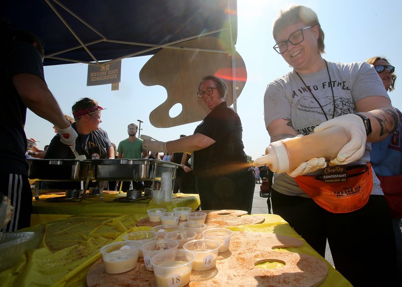 Jera Cobb (right), with the B A Burrito team from Jonesboro puts seasoning on cheese dip at the ninth Annual World Championship Cheese Dip Championship on Oct. 5, 2019, at the Clinton Presidential Center in Little Rock. The team won the award for best booth.