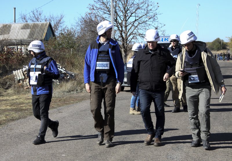Deputy Head of the OSCE Special Monitoring Mission, Mark Etherington, second right, and other members of OSCE walk through a street near a frontline in Petrovske, Ukraine, Wednesday, Oct. 9, 2019. At least one Ukrainian police officer has been injured in scuffles between police and activists who have arrived to the frontline in eastern Ukraine to derail the pullback of government forces. (AP Photo/Alexei Alexandrov) story.lead_photo.caption