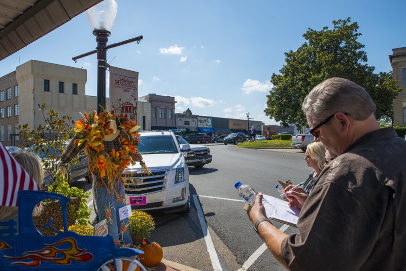 Judges Kevin Russell (front right), Annette Pate (middle), and Amy Wilson score the best fall attractions created by downtown merchants during this year’s Scarecrow Crawl at Magnolia’s square. Pictured is the entry from Bridget's on the Square flower shop. The winner will be announced at tonight’s Second Thursday Market.  Also pictured (left) is Micki Mitchell, director of Magnolia-Columbia County Chamber of Commerce. 