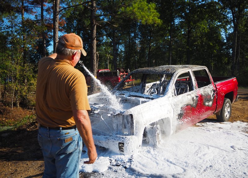 Mike Boyett, chief of the Walker Creek VFD, blankets the burned out, late-model Chevy pickup with liquid foam retardant Wednesday afternoon after the pickup suddenly caught fire while driving down Columbia Rd. 15 in the Bussey-Sharman Community.   