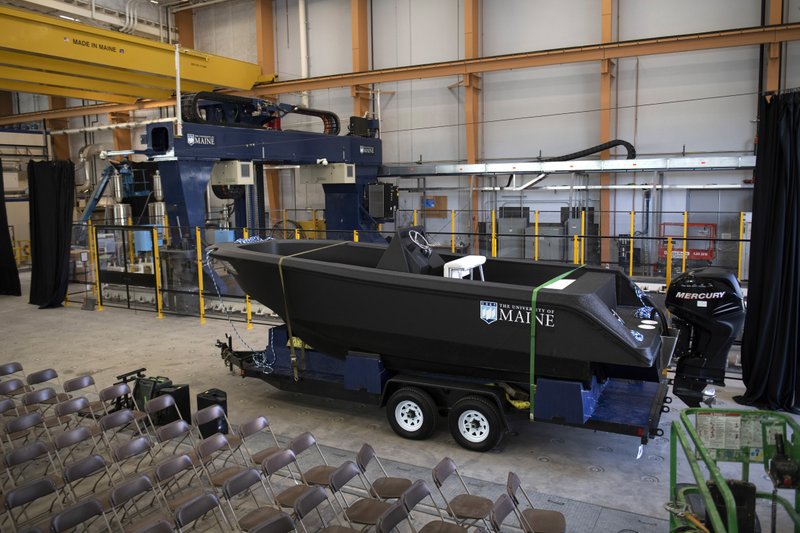 In this Wednesday, Oct. 9, 2019 photo provided by the University of Maine, a 25-foot, 5,000-pound patrol boat, center, that was produced using a large polymer 3D printer, behind left, rests on a trailer on the school's campus, in Orono, Maine. The boat was printed at the school's Composites Center on the world's largest polymer 3D printer. (Ron Lisnet/University of Maine via AP)