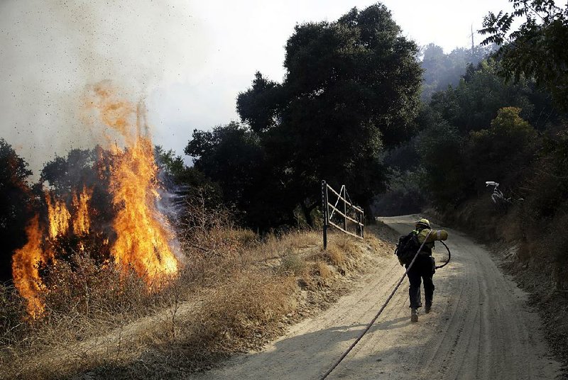 A firefighter runs up a fire road Saturday to hose down flames from a wildfire in Newhall, Calif. 