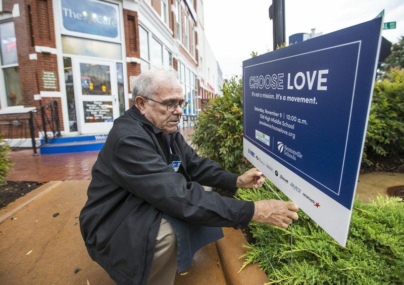 NWA Democrat-Gazette/BEN GOFF &#8226; @NWABENGOFF Jim McCann with the Walmart Museum places a sign Thursday in front of the museum on the Bentonville square. The museum is partnering with Bentonville's School District to promote the Jesse Lewis Choose Love Movement as a method of supporting school safety. The sign advertises an event Nov. 9 at Old High Middle School featuring Scarlett Lewis. Lewis founded the Jesse Lewis Choose Love Movement in honor of her son who was killed in the Sandy Hook Elementary School shooting.