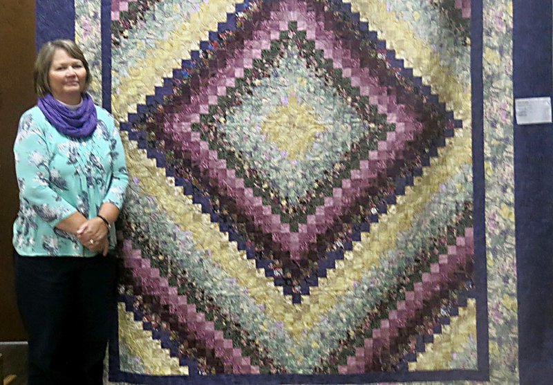 Westside Eagle Observer/SUSAN HOLLAND Peggy Horne, of Jay, Okla., poses beside her Trip Around the World pattern quilt after learning it was chosen as the People's Choice winner Saturday in the quilt show held at the Gravette Civic Center. Horne has recently begun teaching the monthly class meeting of the PieceMakers Quilt Club.