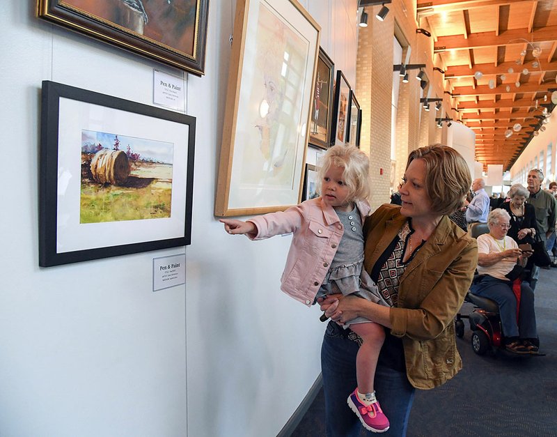 Anilese Withers, 3, and Kelly Withers look over artwork on the opening night of "PEN PEN AND PAINT: The Art of Gary Simmons and Richard Stephens" at the Hot Springs Convention Center on Tuesday. - Photo by Grace Brown of The Sentinel-Record