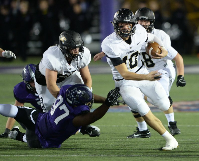 NWA Democrat-Gazette/ANDY SHUPE Bentonville quarterback Ben Pankau (10) carries the ball Friday, Oct. 18, 2019, as he slips out of the grasp of Fayetteville defensive end Melvin Kumwenda (97) during the first half of play at Harmon Stadium in Fayetteville. Visit nwadg.com/photos to see more photographs from the game.