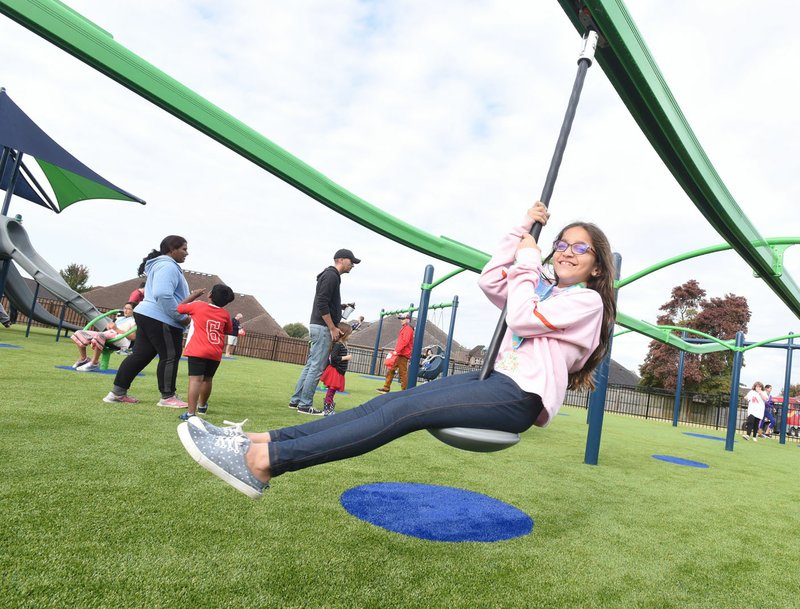 NWA Democrat-Gazette/FLIP PUTTHOFF Noor Adeel, 8, swings on a ride Saturday during the opening of Citizens Park's inclusive playground at the Bentonville Community Center. The playground is designed so children of all abilities can play together, said David Wright, Parks and Recreation director.