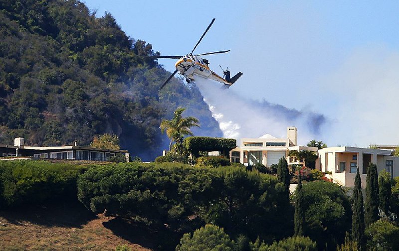 A Los Angeles County Fire Department helicopter drops water Monday as flames from a wildfire threaten homes on a ridgeline in the Pacific Palisades area of Los Angeles. 