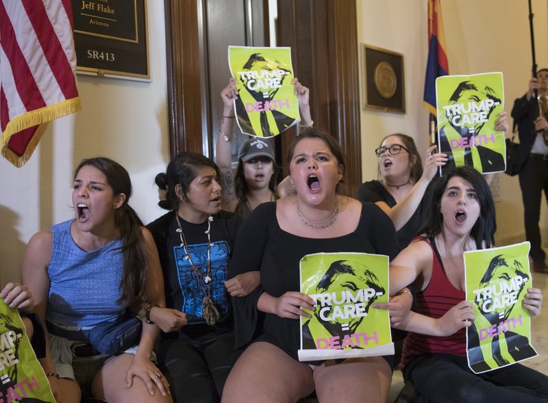 FILE - In this July 10, 2017, file photo, activists protest against the Republican health care bill outside the offices of Sen. Jeff Flake, R-Ariz., and Sen. Ted Cruz, R-Texas on Capitol Hill in Washington. Arizona has quietly suspended its plans to require that about 120,000 people receiving Medicaid benefits work, volunteer or go to school. The state Medicaid program posted a notice on its website saying the work requirements are being delayed &quot;as court cases in other states play out.&quot; The decision is a further setback to efforts by President Donald Trump and his allies in many Republican-led states to put conditions on low-income people seeking taxpayer funded benefits. (AP Photo/J. Scott Applewhite, File)