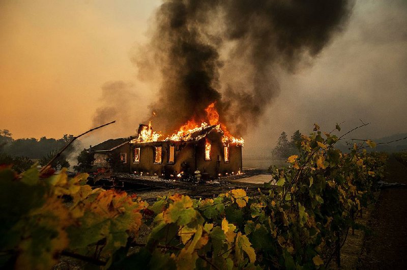 Grape vines frame a burning house Thursday in the Jimtown community in Northern California’s Sonoma County wine country, where a wildfire has forced the evacuation of more than 2,000 people and prompted new electrical blackouts. In Southern California, two wildfires caused 40,000 people to evacuate. More photos at arkansasonline.com/1025wildfire/ 