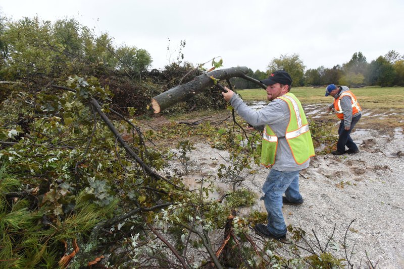 Mike Smyers (left) and Kevin Olson, Rogers city employees with the street department and parks department, pile branches at a city disposal site at the Blossom Way trailhead near Dixieland Road and Price Lane. City crews are hauling tree branches to the site after severe storms toppled trees early Monday.