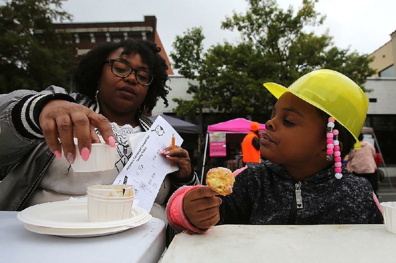 Lacy Higgins, 3, munches on a cornbread fritter Saturday while her mother, Latonya, judges cornbread samples during the ninth  annual Arkansas Cornbread Festival in Little Rock. More photos are available at www.arkansasonline.com/1027cornbread/ 