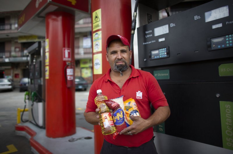 In this Oct. 8, 2019 photo, gas station attendant Leowaldo Sanchez poses with food items he was paid with by motorists: a bottle of cooking oil, a kilogram if rice and a package of corn flour, as he works at the pump in San Antonio de los Altos on the outskirts of Caracas, Venezuela. Bartering at the pump has taken off as hyperinflation makes Venezuela&#x2019;s paper currency, the bolivar, hard to find and renders some denominations all but worthless, so that nobody will accept them. (AP Photo/Ariana Cubillos)