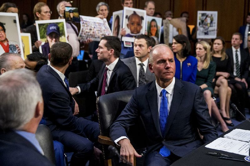 During a Senate Transportation Committee hearing Tuesday in Washington, Boeing executive Dennis Muilenburg (right) looks away  as family members hold up photographs of people killed in two Boeing 737 Max crashes. 