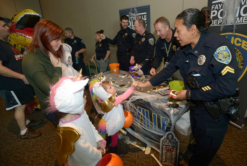 NWA Democrat-Gazette/ANDY SHUPE
Cpl. Julia McKinney (right) with the Fayetteville Police Department gets a high-five Wednesday, Oct. 31, 2018, from Frankie Cole, 3, of Prairie Grove as her sister, Nora Cole, 6; and mother, Kara Cole, watch during the annual Trick or Treat on the Square in the Fayetteville Town Center in downtown Fayetteville. The event is presented by Experience Fayetteville and features booths from local businesses and city departments offering Halloween candy to visitors. Weather forced the event inside.
