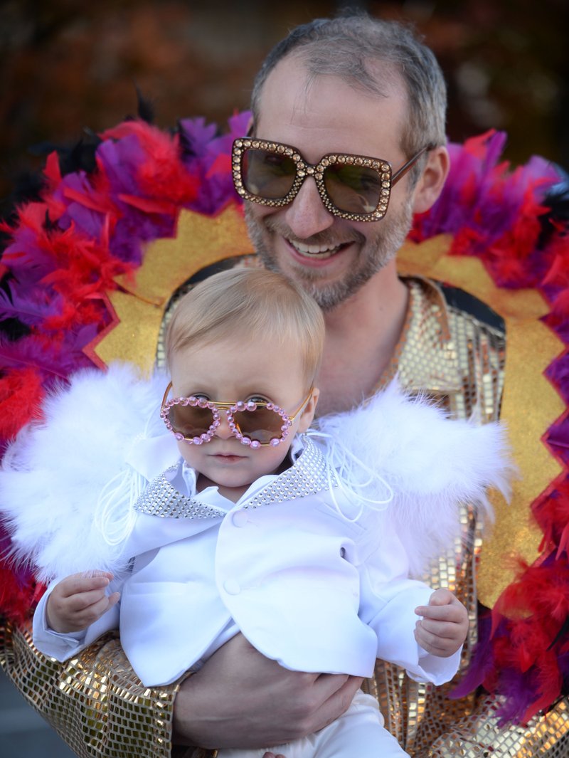Jacob Leonard and his 1-year-old daughter, Jane Leonard, show off their Elton John costumes Thursday during the annual Trick-or-Treat on the Square hosted by Experience Fayetteville. Businesses on the square join city departments in handing out candy to trick-or-treaters. NWA Democrat-Gazette/ANDY SHUPE