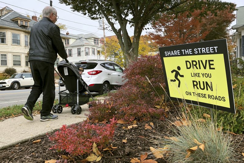 A man pushes a child in a stroller past a sign urging drivers to share the road with runners, walkers and cyclists in Providence, R.I., on Wednesday. Elite marathoner Kaitlin Goodman, of Providence, who suffered a severe injury while jumping out of the way of a distracted driver, recently launched "Safe on the Road," a new campaign to help pedestrians and motorists coexist on the nation's roadways. - AP Photo/William J. Kole