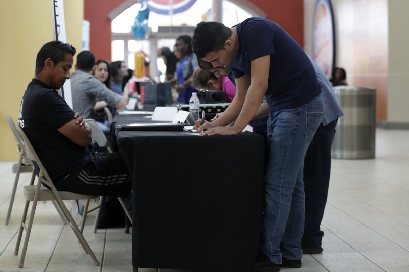 FILE - In this Oct. 1, 2019, file photo Billy Ramos, right, fills out a job application with Adidas during a job fair at Dolphin Mall in Miami. On Friday, Nov. 1, the U.S. government issues the October jobs report. (AP Photo/Lynne Sladky)
