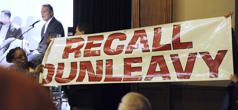 FILE - In this March 26, 2019, file photo, protesters unfurl a banner as Alaska Gov. Mike Dunleavy speaks during a roadshow with Americans for Prosperity in 49th State Brewing Company in Anchorage, Alaska. A fight is brewing over whether Dunleavy, a Republican who took office in Dec. 2018, should be recalled. Critics say he's incompetent and has recklessly tried to cut spending while supporters see a politically motivated attempt to undo the last election. (Bill Roth/Anchorage Daily News via AP, File) story.lead_photo.caption