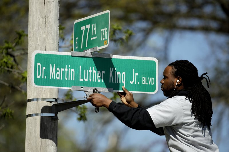 FILE - In this April, 20, 2019, file photo, public works employee Jerry Brooks changes a street sign from The Paseo to Dr. Martin Luther King Jr. Blvd. in Kansas City, Mo. More than 50 years after King was assassinated, the city's efforts to honor the civil rights leader has met opposition from citizens opposed to the renaming of The Paseo, one of the city's iconic boulevards. (AP Photo/Charlie Riedel, File)