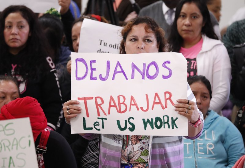An attendee at the House Homeland Security Committee field hearing at Tougaloo College in Jackson, Miss., holds a sign written in English and Spanish, stating "Let US work" Thursday, Nov. 7, 2019. The hearing concerned the Aug. 7, 2019 ICE raids throughout Mississippi which resulted in nearly 700 workers being arrested at seven chicken processing plants. (AP Photo/Rogelio V. Solis)