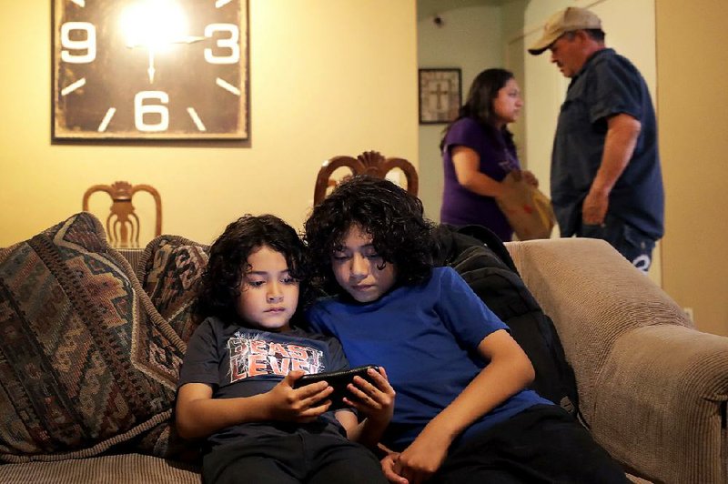 John Diaz (left) and his brother Joseph Diaz watch videos Thursday as their parents, Karina Ruiz and Humberto Diaz prepare dinner at their home in Glendale, Ariz. Karina is enrolled in the Deferred Action for Childhood Arrivals program. 