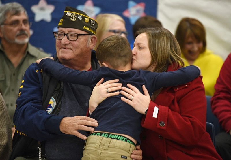 Jay Kidd, a first-grader at Smith Elementary School, receives a hug Monday from his mother, Deannee (right), and his grandfather, retired Navy veteran Clarence J. Diett, during the We Honor You program dedicated to veterans at the Springdale school. The program included the recognition of veterans, a slide show, and musical performances by students and the teachers. NWA Democrat-Gazette/DAVID GOTTSCHALK