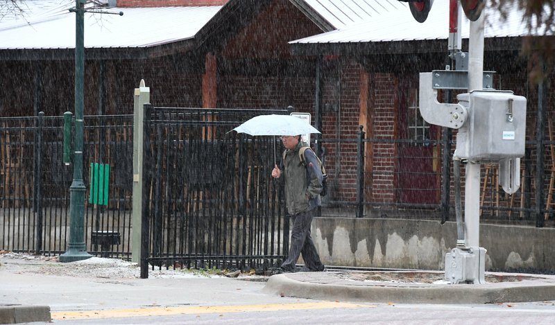 NWA Democrat-Gazette/J.T. WAMPLER A pedestrian walks along Dickson Street in Fayetteville on Monda as sleet and snow fall. The National Weather Service is calling for clear skies the rest of the week with overnight lows in the teens and 20s.