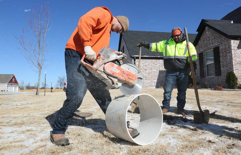 NWA Democrat-Gazette/DAVID GOTTSCHALK Chad Murphy (left) uses a chop saw to cut an 18-inch polyinyl chloride pipe Tuesday with Jason Wedel, both with Springdale Water Utilities, to raise a meter box.