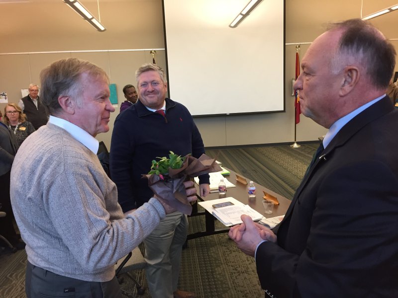 NWA Democrat-Gazette/DAVE PEROZEK Michael Pearce (left) accepts a plant from Joe Spivey (right) chairman of the Northwest Arkansas Community College Board, during a meeting Tuesday as fellow trustee Mark Scott looks on. Spivey presented the gift upon announcing Pearce, the board's Zone 7 representative, is resigning at the end of this year.