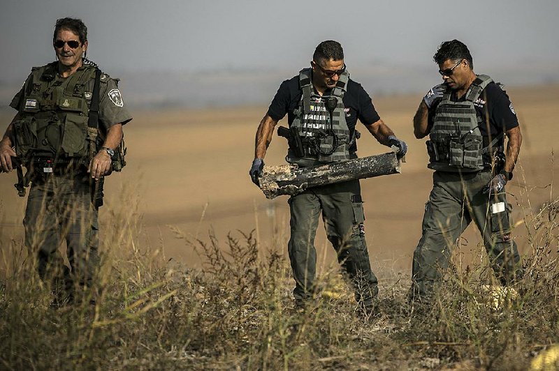 Israeli police bomb disposal officers remove a rocket Wednesday that was fired from the Gaza Strip into farmland near the Gaza border. More photos are available at arkansasonline.com/1114israel/ 