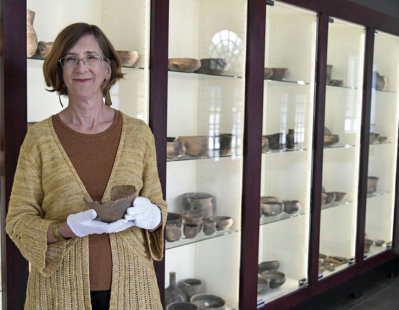 Mary Beth Trubitt, Ph.D. and professor at Henderson State University displays a piece of Native American pottery as she stands in front of a display case at the university. -Photo by Grace Brown of The Sentinel-Record