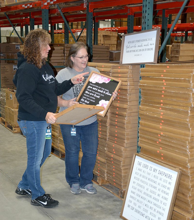 Janelle Jessen/Siloam Sunday Sherri Brooker (left), DaySpring Outlet Store manager and warehouse sale coordinator, and Terri Black, store cashier and warehouse sale site manager, unpacked decorative wall hangings for the upcoming annual warehouse sale.