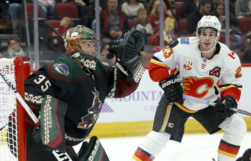 Arizona Coyotes goaltender Darcy Kuemper (35) reaches out to make a glove save on a shot as Calgary Flames center Sean Monahan (23) looks on during the first period of Saturday's game in Glendale, Ariz. - Photo by Ross D. Franklin of The Associated Press