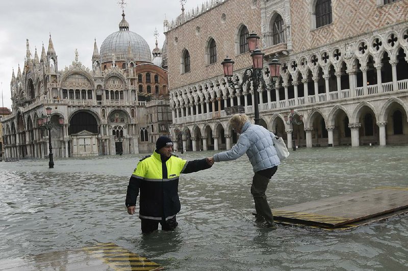 A city worker helps a woman who decided to cross St. Mark’s Square on a gangway, in spite of prohibitions against it, Sunday in Venice, Italy. More photos are available at arkansasonline.com/1118venice/ 