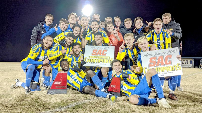 Photo courtesy of JBU Sports Information The John Brown men's soccer team celebrates with championship banners after defeating Science and Arts (Okla.) 1-0 on Saturday to win the Sooner Athletic Conference tournament championship at Alumni Field.